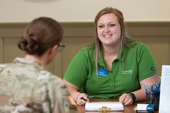 A woman in a green shirt is sitting at a table with a woman in a camouflage shirt.